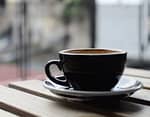 selective focus photography of black ceramic tea mug and plate on brown wooden table during daytime