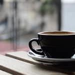 selective focus photography of black ceramic tea mug and plate on brown wooden table during daytime