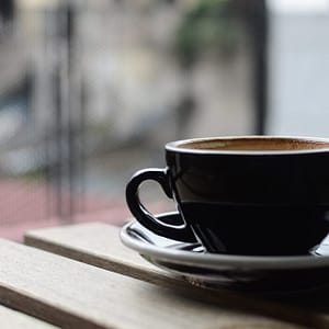 selective focus photography of black ceramic tea mug and plate on brown wooden table during daytime